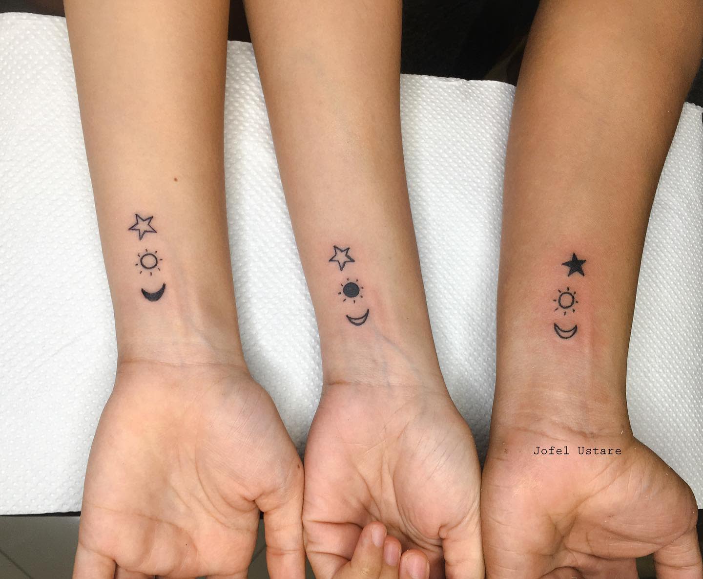 Matching wrist tattoos featuring a star, sun, and crescent moon, symbolizing unity and balance between light and dark